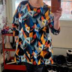 Henkilö värikkäässä kissakuosisessa mekossa peilin edessä